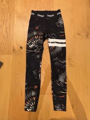 Mönstrade leggings från Stronger XS - Säljer ett par leggings från Stronger i storlek XS. Hög midja med logga i midjebandet och två vita ränder på ena benet. Fina och sköna, perfekta för träning. Väldigt bra skick! Säljer pågrund av att jag inte använder de. 
