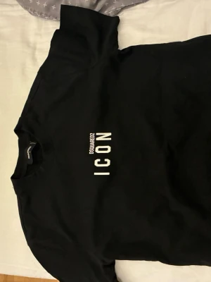 Svart Dsquared2 ICON t-shirt - Snygg svart t-shirt från Dsquared2 med det ikoniska vita 'ICON'-trycket på bröstet. Klassisk rund hals och korta ärmar. Tillverkad i mjuk bomull som känns skön mot huden. Perfekt för dig som vill ha en stilren och trendig look.