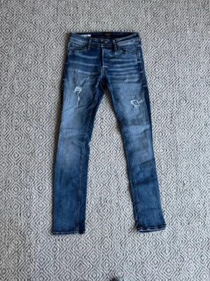 Blå slitna skinny jeans - Säljer ett par blå skinny jeans med slitningar och hål på låren och knäna. Jeansen har en tvättad look och fem klassiska fickor. Perfekta för en avslappnad och trendig stil. Skriv för mer info 