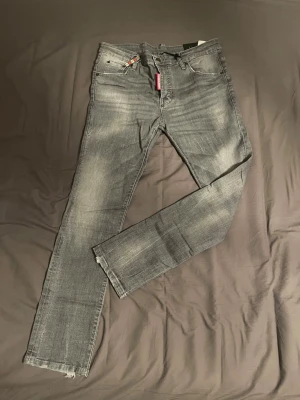Grå slim fit jeans från Dsquared2 - Snygga grå slim fit jeans från Dsquared2 med slitna detaljer och klassisk femficksdesign. Jeansen har en diskret tvättad look och en röd etikett vid gylfen. Perfekta för en trendig och avslappnad stil.