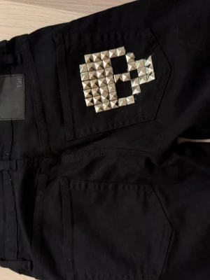 Svarta jeans med döskalle studs - Svarta jeans i rak modell med cool döskalle av silvriga studs på bakfickan. 