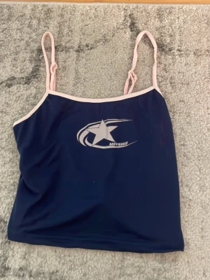 Mörkblå linnetopp med stjärntryck - Snygg mörkblå linnetopp  med vitt stjärntryck framtill och ljusrosa smala axelband. Toppen har en croppad passform och är perfekt för en avslappnad look. Materialet känns mjukt och stretchigt.