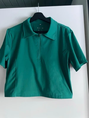 Grön croppad half zip topp H&M Move - Snygg grön croppad topp från H&M Move med korta ärmar och krage. Toppen har en half zip-dragkedja framtill och är gjord i ett stretchigt syntetmaterial som passar perfekt till träning eller sportiga outfits. Liten i storlek 