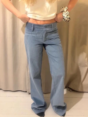 Blåa bootcut jeans med ränder - Snygga blåa bootcut jeans med tunna vita vertikala ränder. Jeansen har låg midja och vida ben, vilket ger en retro och avslappnad vibe. Perfekta för dig som gillar en trendig och bekväm stil.