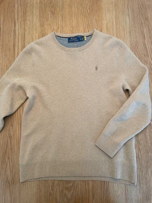 Ralph Lauren tröja - Beige kashmir tröja från Polo Ralph Lauren med  diskret broderad logga på bröstet, rund halsringning och ribbade muddar vid ärmslut och nederkant. Perfekt för en stilren och enkel look. Står strl XL men passar som en S eller XS. Inga defekter.