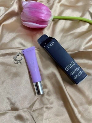 Dior Addict Lip Glow Butter lila - Säljer ett Dior Addict Lip Glow Butter i en snygg lila tub med silverfärgat lock och en Dior-charm. Läppbalsamet har en modern och lyxig design, perfekt att ha i väskan. Förpackningen är elegant och känns exklusiv, och färgen på tuben sticker verkligen ut.