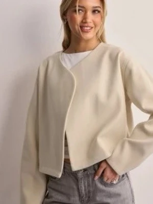 Beige vår jacka med omlott - Trendig beige jacka med omlott-design och lång ärm. Modellen är kort och har en stilren, minimalistisk look. Perfekt att matcha med jeans eller kjol för en clean outfit.