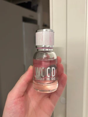 Dsquared2 Wood parfym 30ml - Fräsch parfym från Dsquared2 i serien Wood. Flaskan är genomskinlig med silverfärgad kork och rosa detaljer. Parfymen har en lätt rosa ton och modern design med tydlig logga på framsidan. Perfekt för dig som gillar stilrena och trendiga dofter.