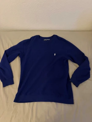 Blå stickad tröja från Ralph Lauren - Mörkblå stickad tröja från Ralph Lauren med rund halsringning och diskret logga broderad på bröstet. Tröjan har långa ärmar och en klassisk, enkel design som passar till det mesta. Perfekt för lager på lager och stilrena outfits.