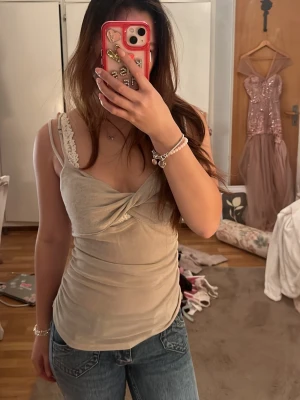 Beige omlott linnetopp med smala band - Snygg beige linnetopp med omlottdetalj framtill och smala axelband. Toppen har en lätt glittrig yta och sitter figurnära. Perfekt att styla med jeans eller kjol för en trendig look.