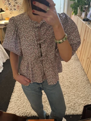 Blommig blus från Ganni - Supersöt blus med småblommigt mönster i lila, rosa och vitt. Puffiga korta ärmar och volang nedtill. I jätte fint skick. 