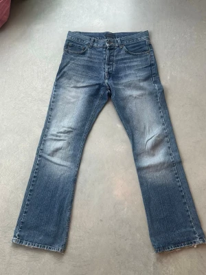 Blå bootcut jeans TDK - Säljer ett par klassiska blå bootcut jeans från TDK med slitningar framtill och bakfickor. Perfekta för en avslappnad och trendig look. Har tyvärr ett litet hål nästan i gylfen se bild 4. Men det är inte svårare än att bara sy igen. 