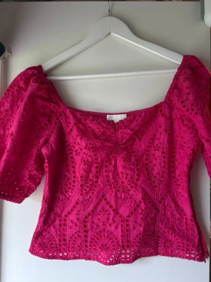 Rosa broderad blus med puffärm - Supersöt rosa blus med broderade detaljer och puffärmar. Toppen har en fyrkantig ringning och är tillverkad i bomull med spetsmönster. Perfekt för dig som vill ha en färgstark och trendig topp med romantiska vibbar.