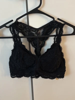 Svart spetsbralette - Snygg svart bralette i spets med dekorativt mönster och racerback-rygg från Cubus. Bh:n har breda axelband och mjuka kupor. Perfekt under linnen eller toppar där spetsen får synas. Gåva vid köp!🎁