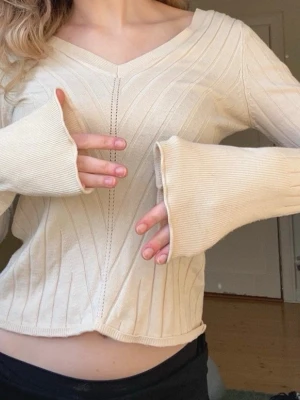 Beige ribbad långärmad topp - Säljer en beige ribbad topp med v-ringning och långa ärmar. Tröjan har en snygg söm framtill och extra långa ärmar som ger en chill vibe. Materialet känns mjukt och stretchigt, perfekt till jeans eller kjol.