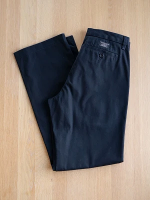 Svarta chinos från Banana Republic 30/32 - Snygga svarta chinos från Banana Republic med klassisk rak passform. Byxorna har sidofickor, bakficka med knapp och bälteshällor. Tillverkade i mjukt bomullstyg med dragkedjegylf och knappstängning. Perfekta för en clean och stilren look.