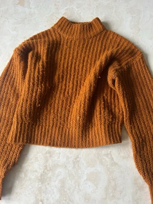 Orange stickad polotröja - Säljer en stickad tröja i snygg orange färg. Tröjan har hög krage, långa ärmar. Snygg till hösten när det blir lite kallare,den är även väldigt varm. Materialet känns mjukt och värmande.