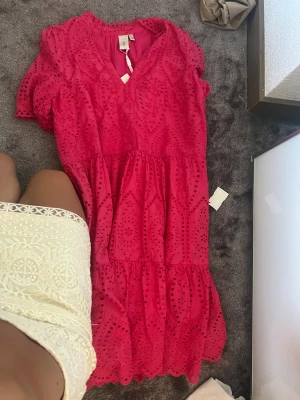 Rosa klänning från YAS i bomull - Superfin rosa klänning från YAS i ekologisk bomull. Klänningen har v-ringning, korta puffärmar och broderade detaljer över hela tyget. Den har en volangig kjol och är perfekt för sommarens alla tillfällen.