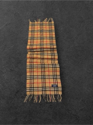 Beige rutig halsduk från Burberry - Klassisk beige halsduk från Burberry med ikoniskt rutmönster i svart, vitt och rött. Halsduken har fransar i båda ändar och är tillverkad i mjuk ull. Perfekt accessoar för att lyfta din outfit med en tidlös och lyxig känsla.
