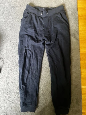 Svarta mjukisbyxor från 157 - Ett par svarta mjukisbyxor från 157 med resår i midjan och dragsko. Byxorna har två sidofickor och ribbade muddar vid bensluten. Perfekta för chill dagar eller när du vill vara extra bekväm. Vid frågor skriv till mig priset kan diskuteras 