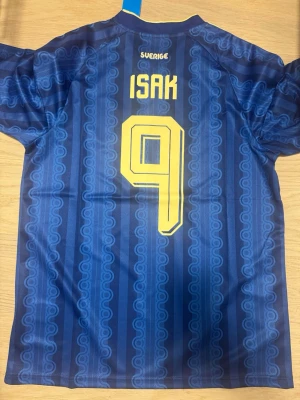 Blå Sverige fotbollströja Isak 9 - Säljer en blå Sverige fotbollströja från Adidas med Isak och nummer 9 på ryggen. Tröjan har gula detaljer, Sveriges landslagsemblem på bröstet och klassiskt Adidas-märke. Tillverkad i lätt och ventilerande material, perfekt för fotbollsträning eller match.