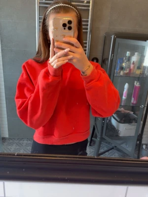 Röd sweatshirt  - Säljer en röd croppad hoodie med oversized passform och breda muddar vid ärmsluten. Hoodien är enkel utan tryck eller logga och har en mjuk insida som gör den skön att bära. Perfekt för en chill och avslappnad stil.