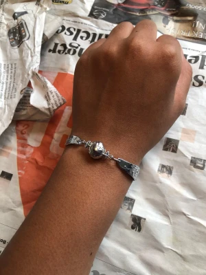 Silverfärgat armband med pärldetalj - Snyggt armband i silverfärg med en rund (plast) pärldetalj i mitten och två bestickskaft. Armbandet har en modern och stilren design som passar till många olika looks. Perfekt accessoar för dig som gillar enkla men unika smycken.