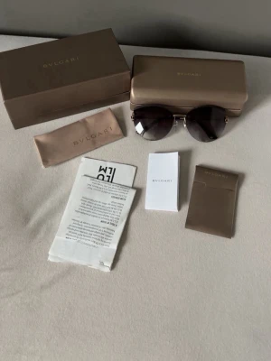 Bvlgari runda solglasögon svart/guld - Snygga solglasögon från Bvlgari med rund form och tunna guldfärgade detaljer. Glasen är mörkt tonade i svart och ger en lyxig känsla. Kommer med originalfodral, putsduk och certifikat. Perfekta för dig som vill ha en exklusiv accessoar. ((ÄKTA, KVITTO FINNS))