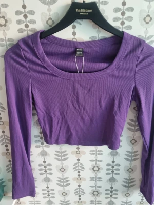 Lila ribbad croppad topp - Trendig lila croppad topp med lång ärm och ribbad struktur. Toppen har en rundad urringning och är perfekt för att styla med höga jeans eller kjol. Enkel men snygg design som passar till många olika looks.