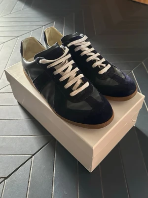Navy GATs - Snygga mörkblå sneakers med vita skosnören och detaljer i både mocka och slätt läder. Yttersulan är i gummi och insidan är ljus. Klassisk låg modell som passar till många olika stilar. Hör av er vid frågor!