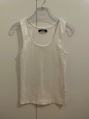 Vit linnetopp från BikBok - Klassisk vit linnetopp från BikBok i mjuk bomull. Modellen är ärmlös med rundad halsringning och har en enkel, clean look som passar till allt. Perfekt basplagg för din garderob och lätt att styla med olika outfits.