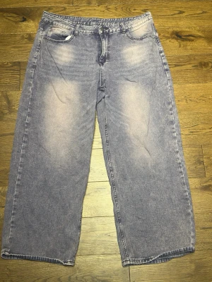 Lila wide leg jeans - Säljer ett par lila jeans med breda ben och hög midja. Jeansen har en tvättad look med ljusare partier framtill och baktill, klassiska fem fickor och dragkedja med knapp. 