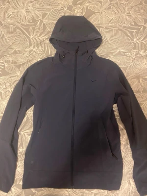 Nike vindjacka - Snygg mörkblå hoodie från Nike med hel dragkedja framtill och två fickor med dragkedja. Tröjan har justerbar huva med snören och diskret Nike-logga på bröstet. Perfekt för en sportig och avslappnad stil.