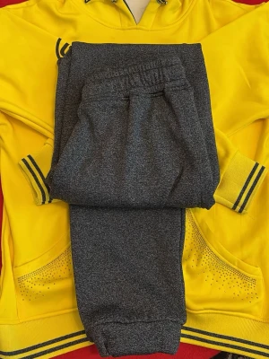 Gul hoodie & grå mjukisbyxor set - Säljer ett mysigt loungewear-set med en gul hoodie med svarta detaljer och fickor med små stenar samt ett par mörkgrå mjukisbyxor med resår i midjan och benslut. Perfekt för chill dagar hemma eller när du vill vara bekväm men ändå snygg.