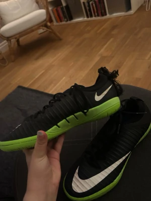 Nike inomhus fotbollsskor - Säljer ett par snygga Nike fotbollsskor i svart med limegrön sula och vit swoosh-logga. Skorna har låg profil, snörning och ribbad ovansida för bättre bollkontroll. 