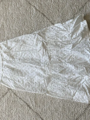 Vit broderad kjol från Lindex - Söt vit kjol från Lindex med broderade detaljer och elastisk midja. Kjolen har ett hålmönster som ger en luftig känsla och passar perfekt till varmare dagar. Enkel att matcha med olika toppar för en fräsch look.