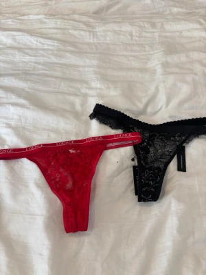 Två oanvända spetsiga trosor från Lounge - Säljer två snygga trosor från Lounge, en röd och en svart. Båda är i spetsmaterial med blommigt mönster och har bred resår med Lounge-logga. Den röda har en sportig look medan den svarta är mer klassisk och elegant. Båda är oanvända med lappen kvar 