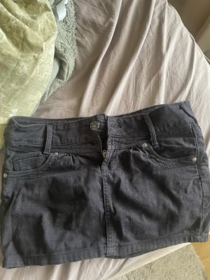 Svart jeanskjol från Lefties - Säljer en svart kort jeanskjol från Lefties i storlek 36. Kjolen har en fin design på fickorna 