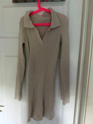 Beige ribbad långärmad klänning - Snygg beige ribbad klänning med lång ärm och v-ringning. Klänningen har en krage och är figurnära med stretchigt material. Perfekt för dig som gillar en stilren och enkel look.