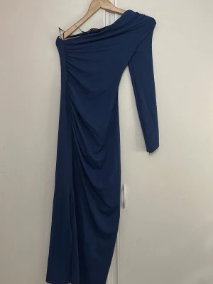 Marinblå oneshoulder klänning Zara - Säljer en marinblå oneshoulder långklänning från Zara. Klänningen har lång ärm på ena sidan och snygg drapering längs sidan för en cool look. Perfekt för dig som vill sticka ut med en unik siluett.