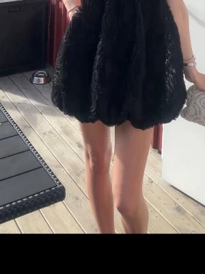 Svart kort klänning med volang - Supersöt svart kort klänning med volangig kjol och ballongformad nederdel. Klänningen har en fluffig struktur och är perfekt för dig som vill sticka ut. Passar dig som gillar trendiga och unika plagg.