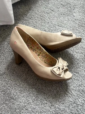 Beige peep toe pumps klackar med rosett - Snygga beiga / rosa klackskor med peep toe och dekorativ rosett framtill. Skorna har en stabil klack och blommigt foder på insidan. Lite slitna här och där som man ser på bilderna. 