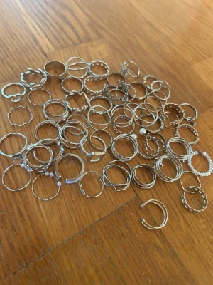 Stort mixat smyckespaket ringar  - Säljer ett stort paket med olika ringar i silverfärgad metall, vissa med pärldetaljer och tvinnade former. Perfekt för dig som gillar att variera dina accessoarer.