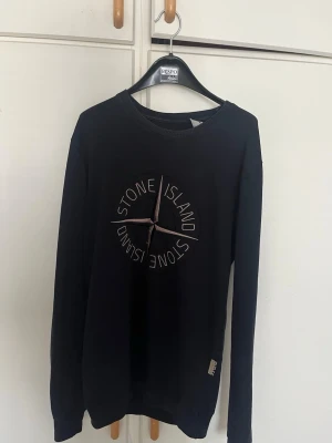 Svart Stone Island sweatshirt pris kan diskuteras - Snygg svart sweatshirt från Stone Island med stort broderat logotyptryck på bröstet. Tröjan har rund halsringning och långa ärmar. Tillverkad i mjukt bomullsmaterial för en bekväm känsla. Perfekt för en avslappnad streetwear-look.