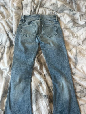 Blå bootcut jeans med slitningar - Säljer ett par ljusblå bootcut jeans med slitningar på knäna och framsidan. Jeansen har två stora framfickor och två bakfickor. Klassisk denimlook med en lätt tvättad finish. Perfekta för en avslappnad och trendig stil.