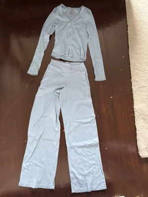 Aim’n Ljusblått ribbat loungewear-set  - Mysigt loungewear-set från Aim’n i ljusblå ribbad trikå. Setet består av en långärmad, figurnära cardigan med knappar framtill och ett par matchande vida byxor med hög midja. 