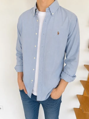 Ljusblå skjorta från Ralph Lauren (M fits S) - Klassisk ljusblå skjorta från Ralph Lauren med button-down krage och broderad logga på bröstet. Skjortan har långa ärmar, vita knappar och är tillverkad i mjuk bomull. Perfekt till jeans eller chinos för en clean och stilren look.