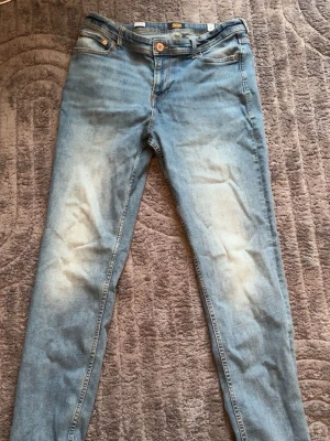 Ljusblå skinny jeans från Jack & Jones - Säljer ett par ljusblå skinny jeans från Jack & Jones med klassisk femficksmodell och slitna detaljer på framsidan. Jeansen har normal midja, dragkedjegylf och patch med logga bak i midjan. Perfekta för en avslappnad och trendig look.