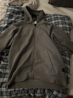 Replay kofta - Säljer en stilren grå hoodie med dragkedja framtill och praktisk huva. Hoodien har en ficka på magen och ribbade muddar vid ärmslut och nederkant. Materialet känns mjukt och bekvämt, perfekt för chill dagar. Liten logga på bröstet för en clean look. Använd 1 gång då den är lite för liten för mig då att den är i princip helt ny