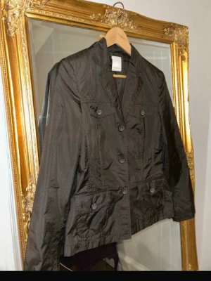 Brun kavaj med fickor - Snygg brun kavaj med fyra framfickor och knappar framtill. Klassisk krage och figurnära passform. Tillverkad i ett lätt bomullsliknande material som ger en avslappnad men ändå stilren look. Perfekt att slänga över en t-shirt eller skjorta.